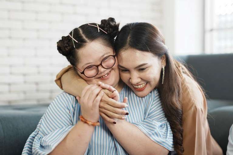 A laughing woman hugging her special needs daughter